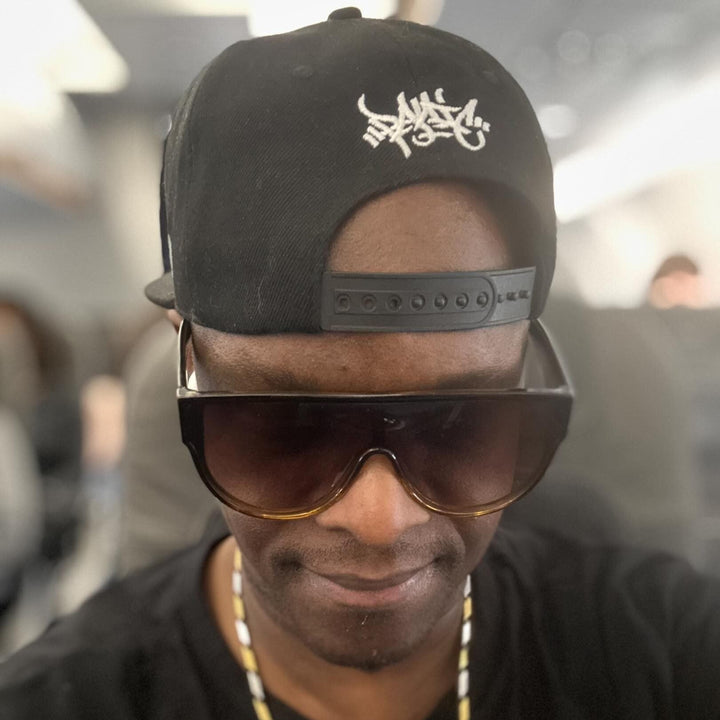 DJ SS in a black Panic 39 tag snapback worn backwards with sunglasses, London