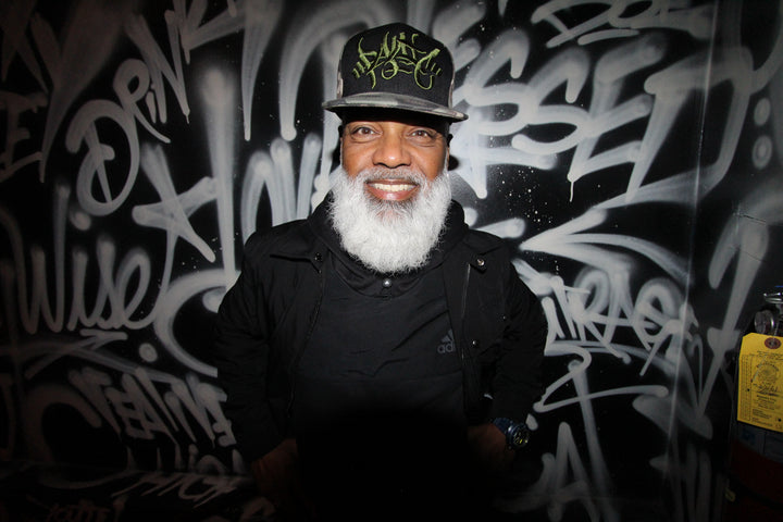 Ray Keith smiling in front of a graffiti-tagged wall at Merge Music, Huntington Beach