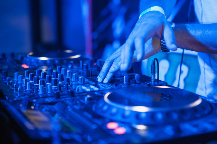 DJ's hands on a mixer and decks under blue club lights