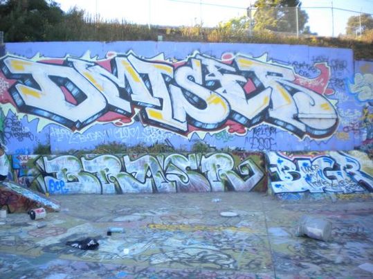 Big graffiti piece on a long wall with throw-ups underneath