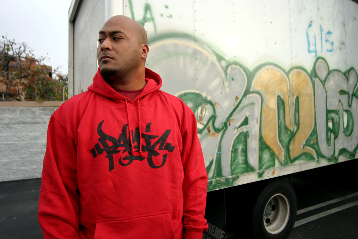 Man in a red Panic 39 tag logo hoodie standing in front of a graffiti-covered box truck